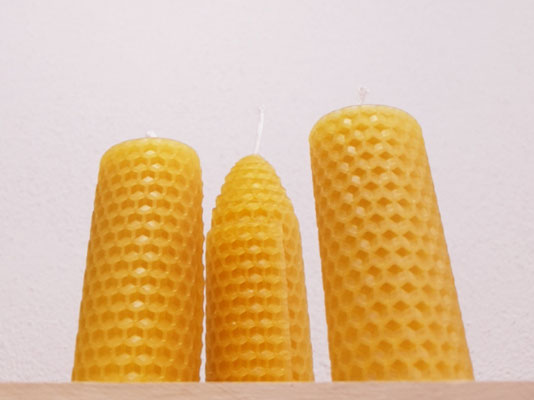 Drei Bienenwachskerzen vor einer weißen Wand.